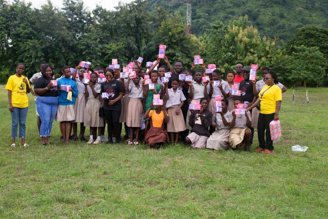 Students and WomenNow facilitators holding packs of menstrual pads outdoors