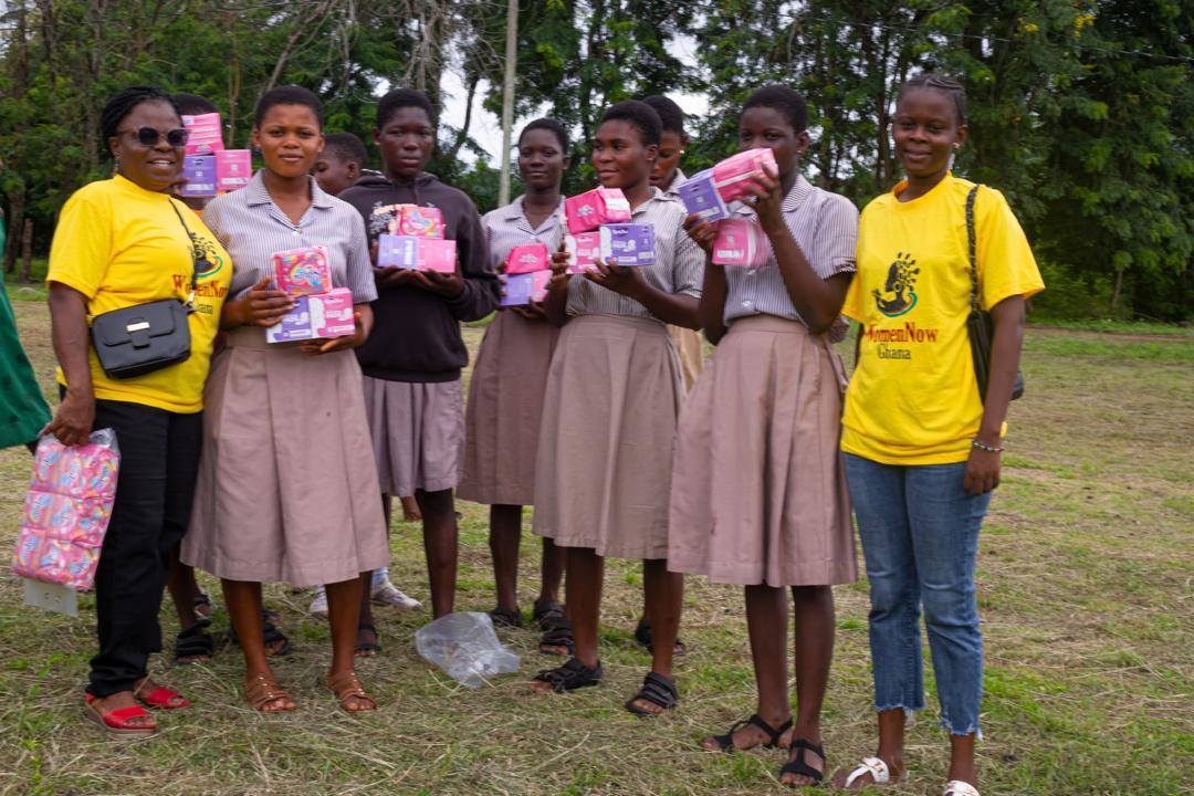 Students holding packs of pads alongside WomenNow facilitators