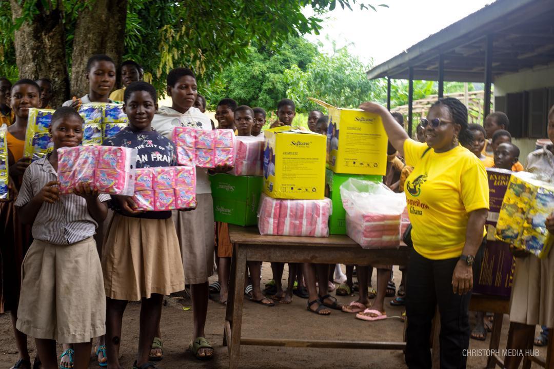 Students and a WomenNow volunteer standing beside boxes and packs of pads