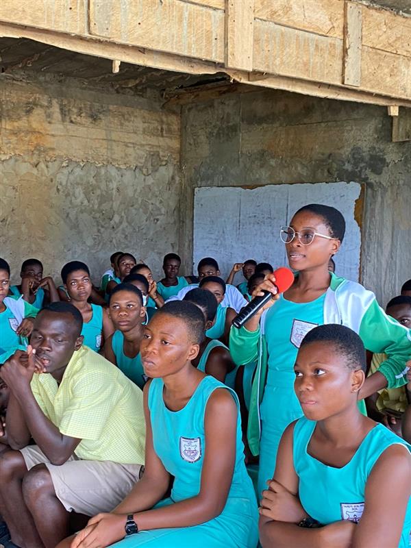 A student speaking into a microphone while her peers listen